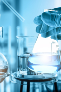 Scientist’s gloved hand holding a laboratory flask containing clear liquid against a blue-lit laboratory background, emphasizing rigorous testing and scientific validation
