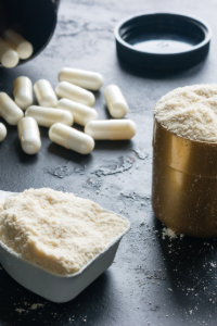 Protein powder in a measuring scoop and container, alongside white supplement capsules on a dark surface, representing bulk supplements for manufacturing